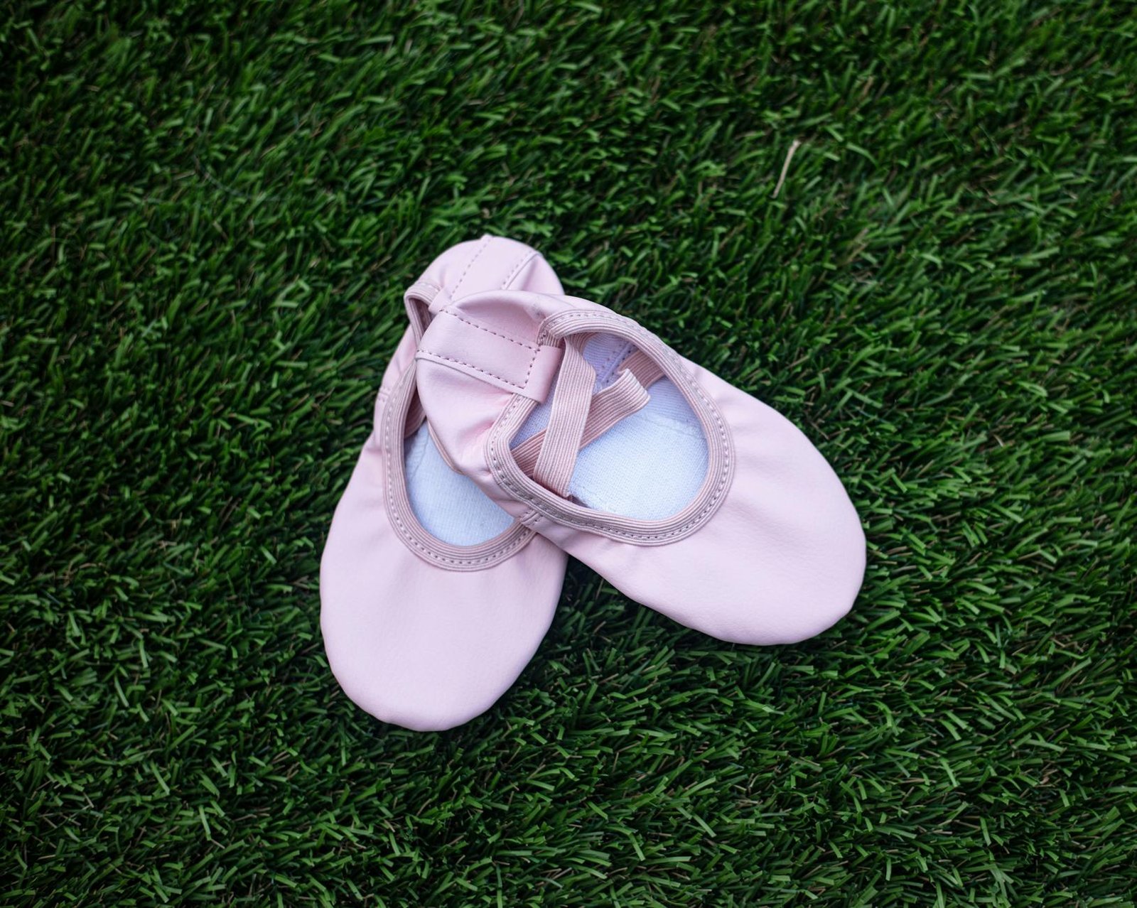 Pair of pink ballet shoes placed neatly on a vibrant green grass surface.