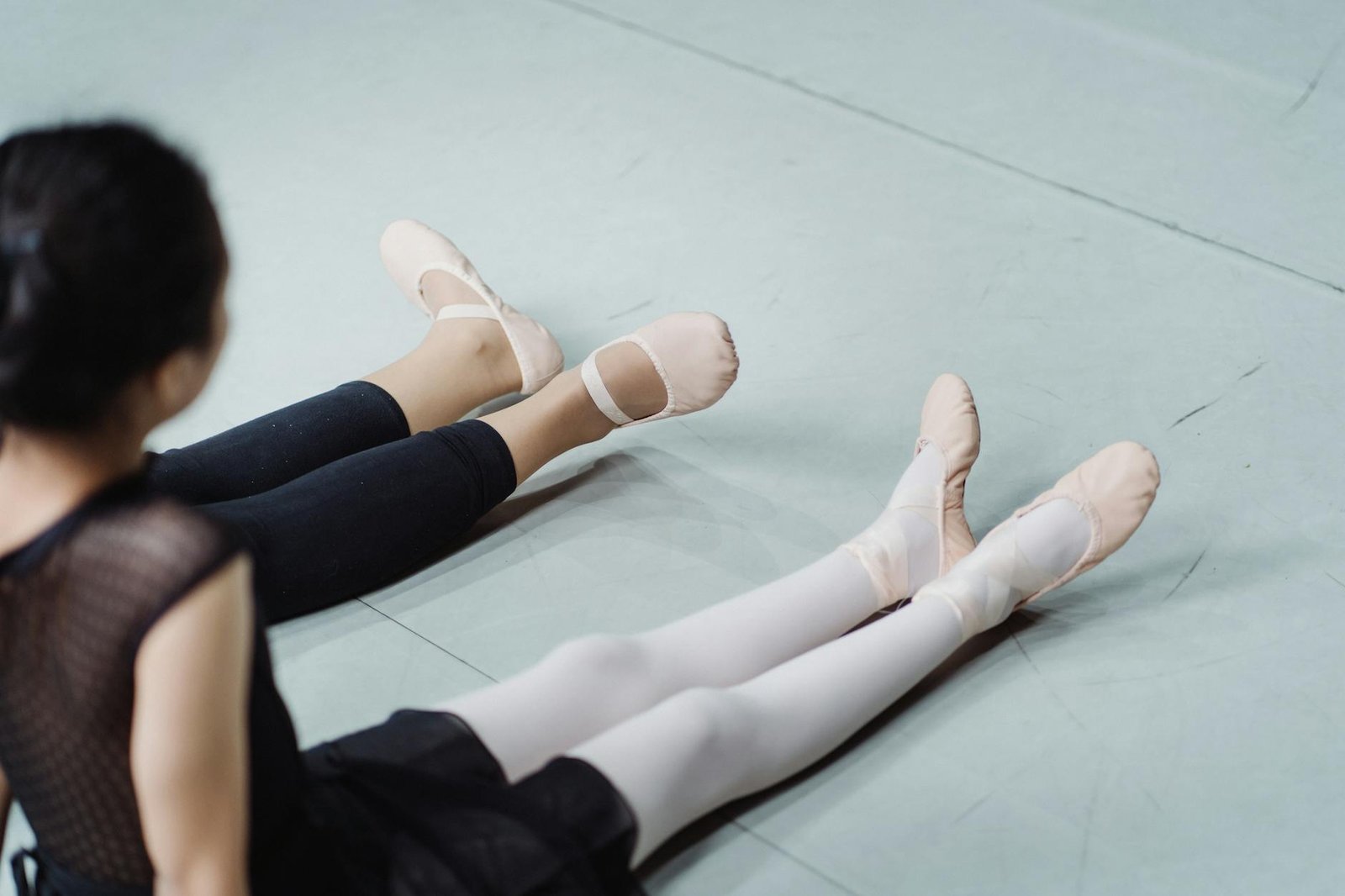 From above back view of crop anonymous instructor with pupil in ballet shoes working out in dancing hall