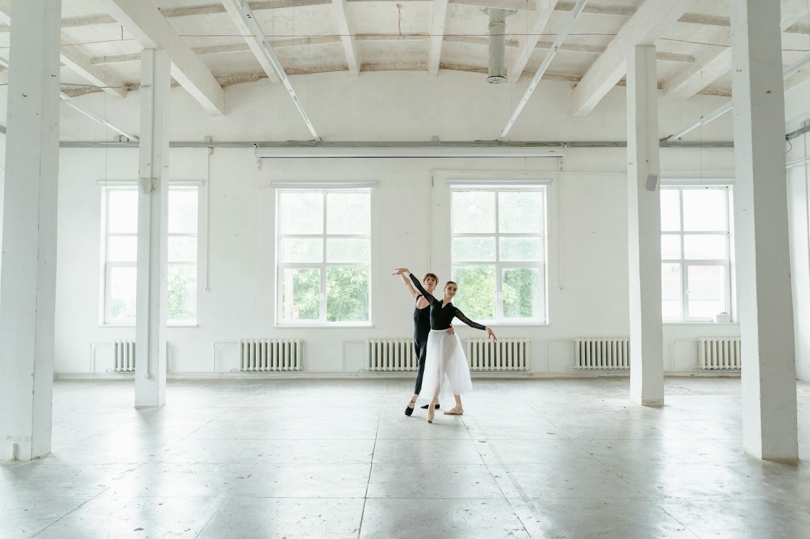 Two ballet dancers gracefully practicing poses in a bright, spacious studio.