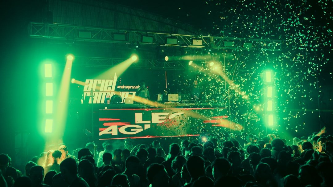 Dj performing for a crowd with green lights and confetti.