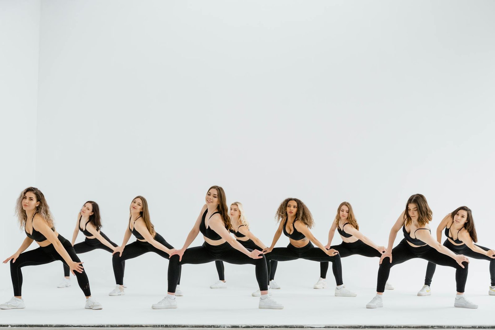 A dynamic group of women performing a synchronized dance routine in sportswear on a white background.