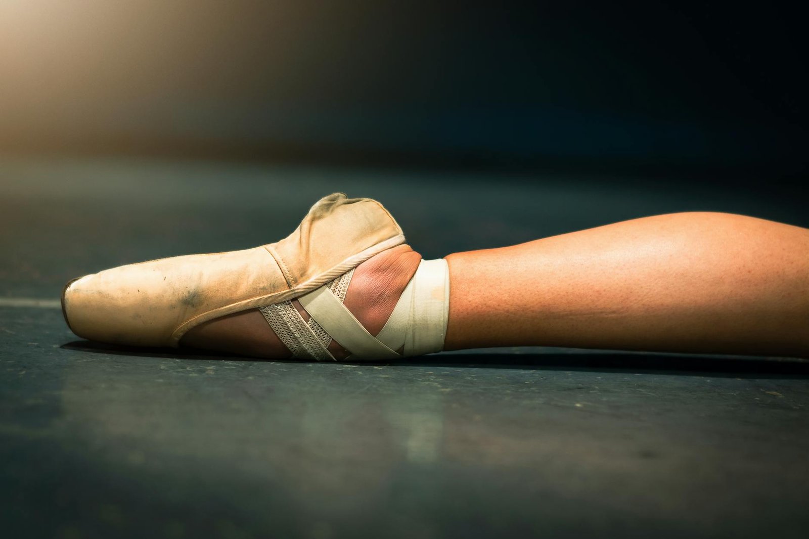 Detailed shot of a ballerina's foot in a pointe shoe on a dance stage floor.
