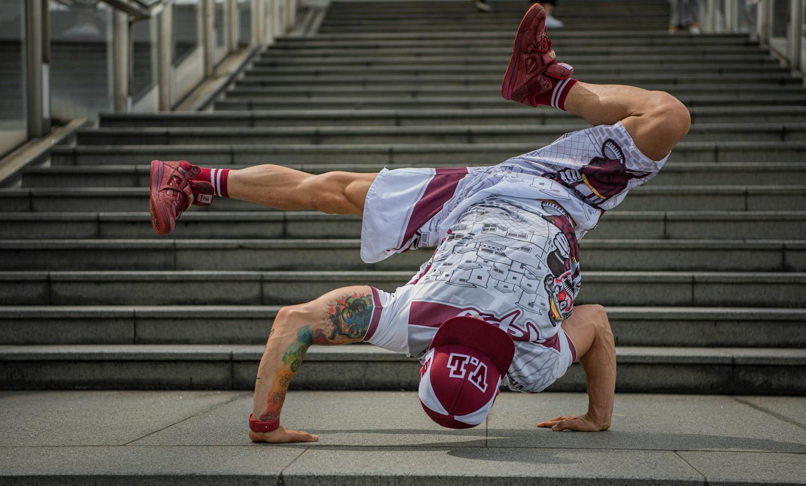 Dynamic breakdancer executing a freeze on city stairs in colorful attire.
