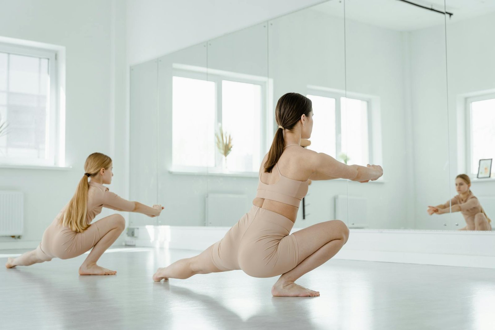 Two women stretching and dancing in a bright studio, reflecting in mirrors.