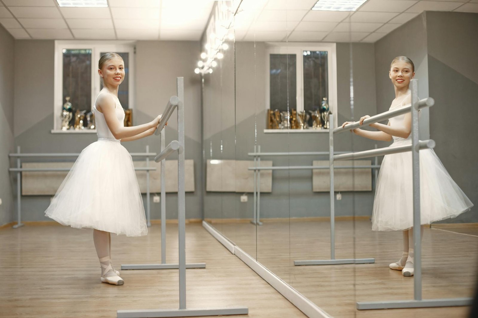 Young ballerina practicing at a ballet barre in a studio, smiling at camera.