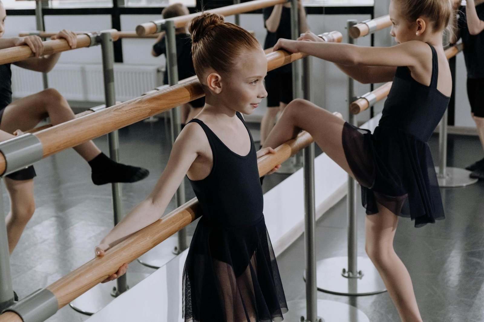 Young ballerinas in a studio practicing ballet techniques at the barre.