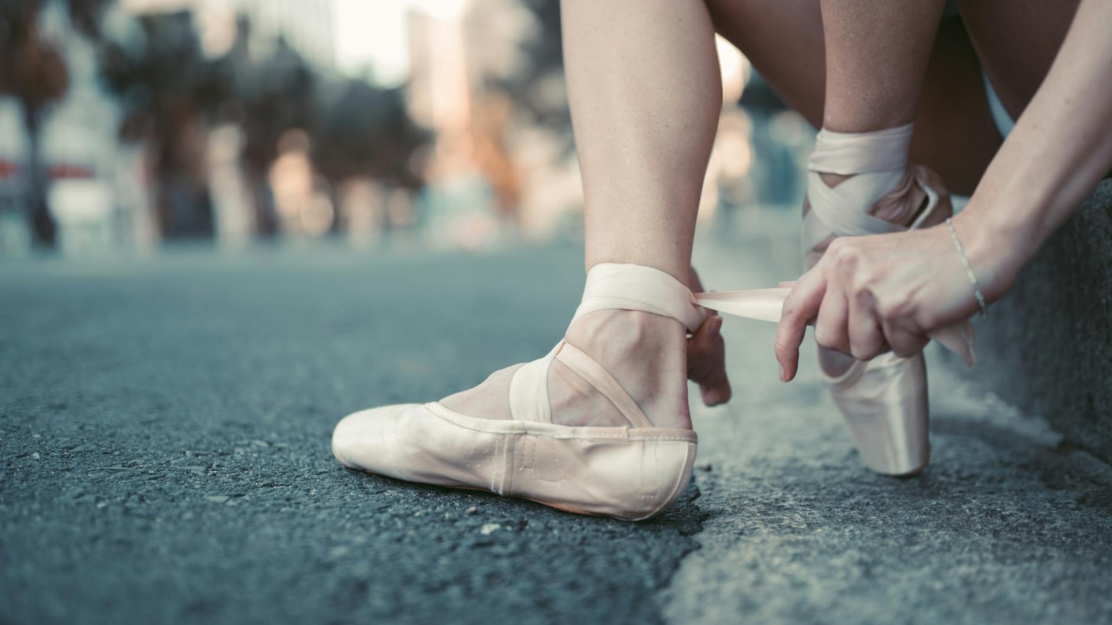 Close-up image of a ballet dancer tying pointe shoes on an urban street.
