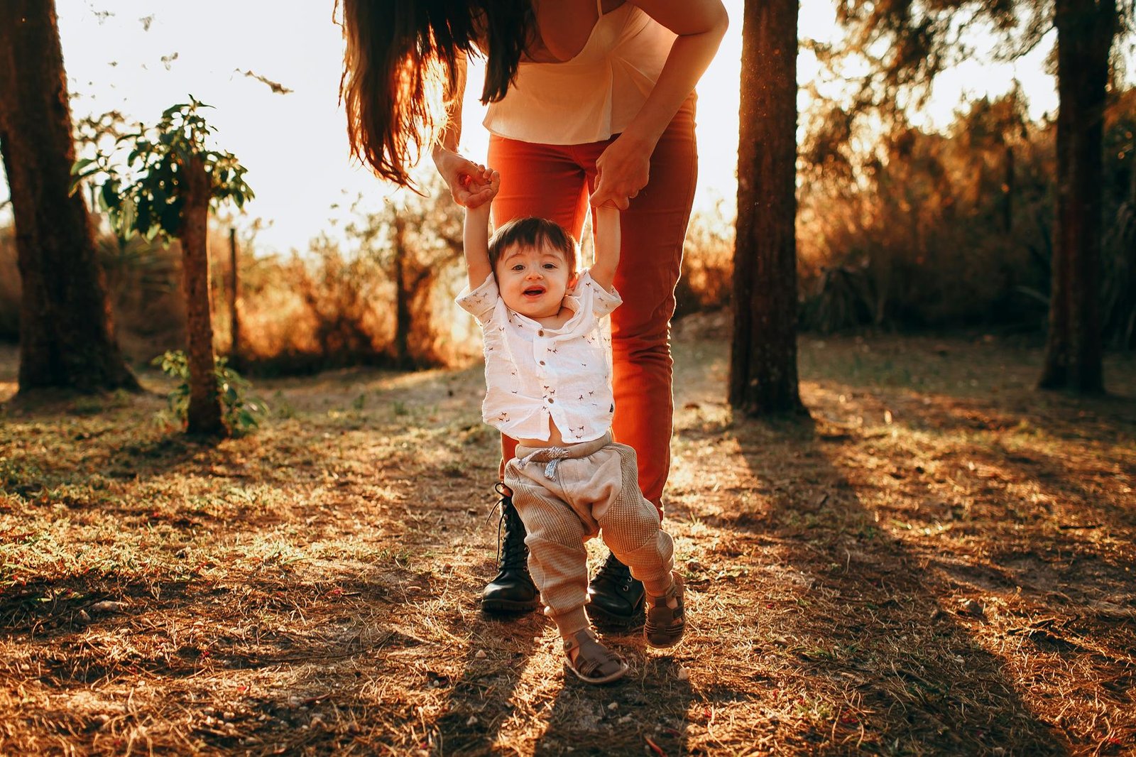 Mother helping her baby walk in a sunlit park, capturing a joyful moment.