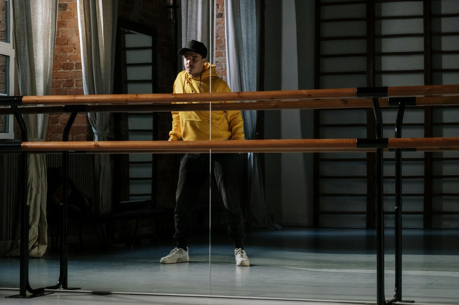 A dancer in a yellow hoodie practicing in a studio with a mirrored wall.