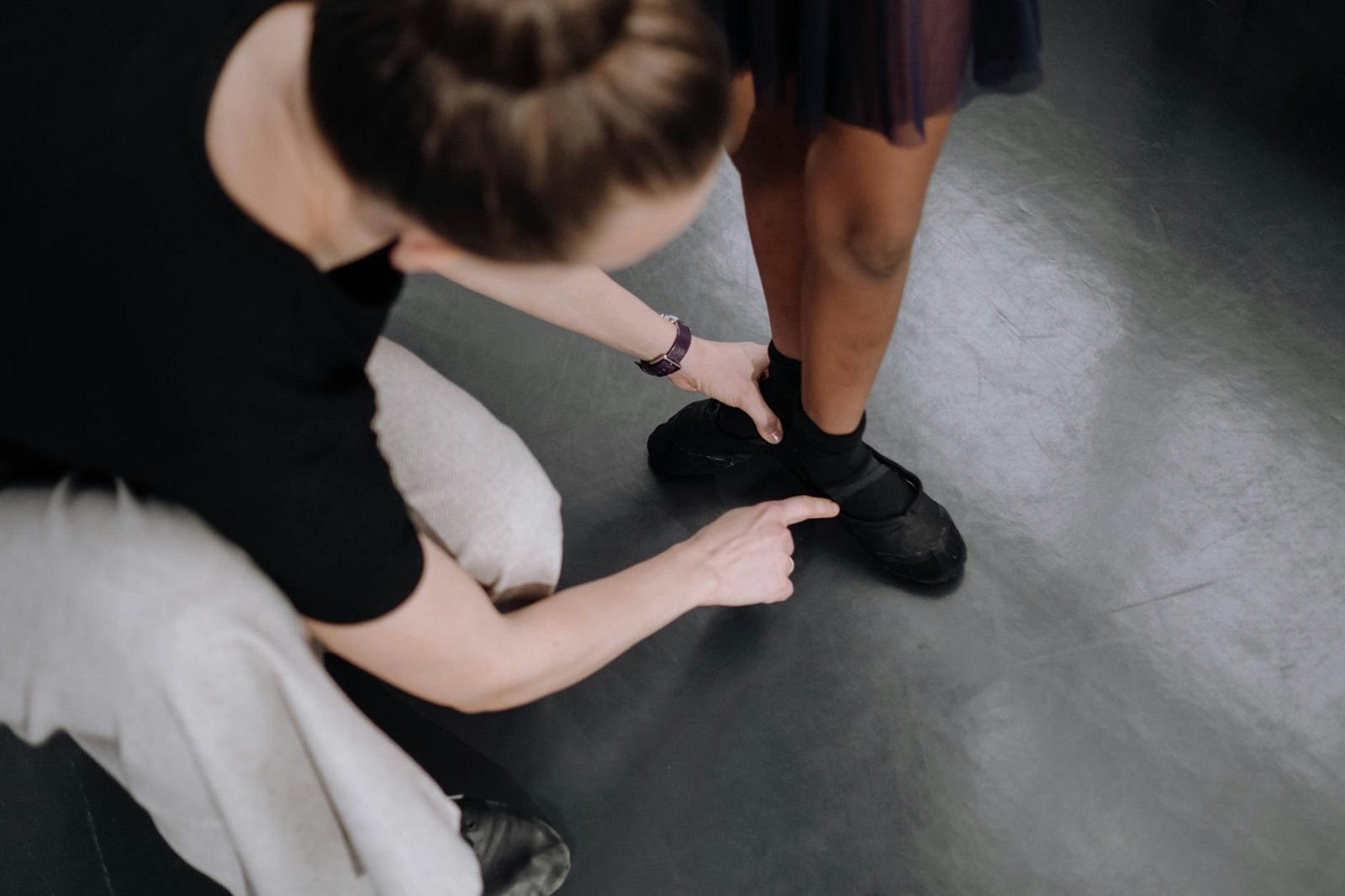 Instructor guides young dancer's foot positioning during ballet practice in a studio.