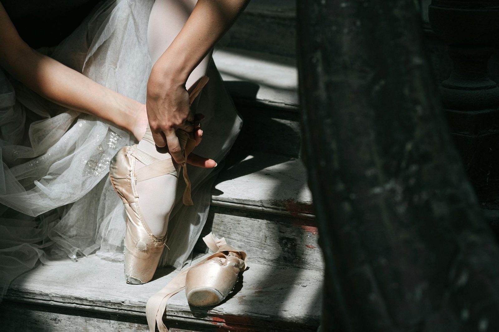 Close-up of a ballerina gracefully tying her pointe shoes on a stairway, capturing the essence of ballet art.