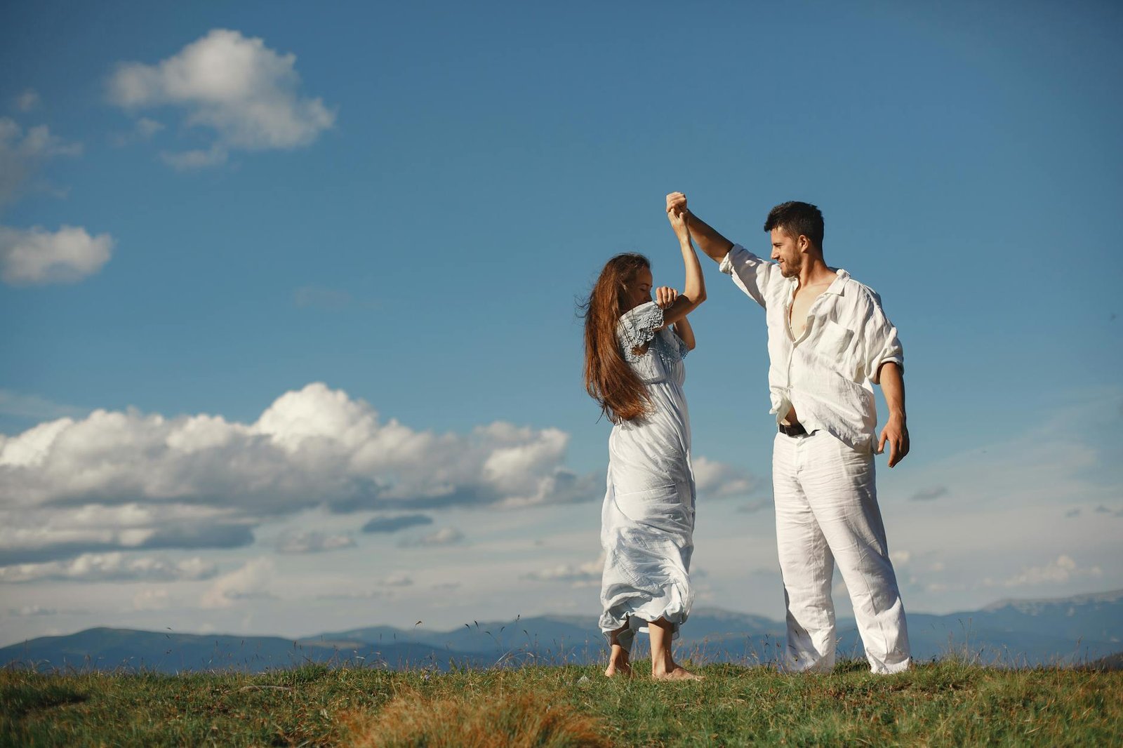 A joyful couple dancing on a grassy hilltop under a bright blue sky, symbolizing love and freedom.
