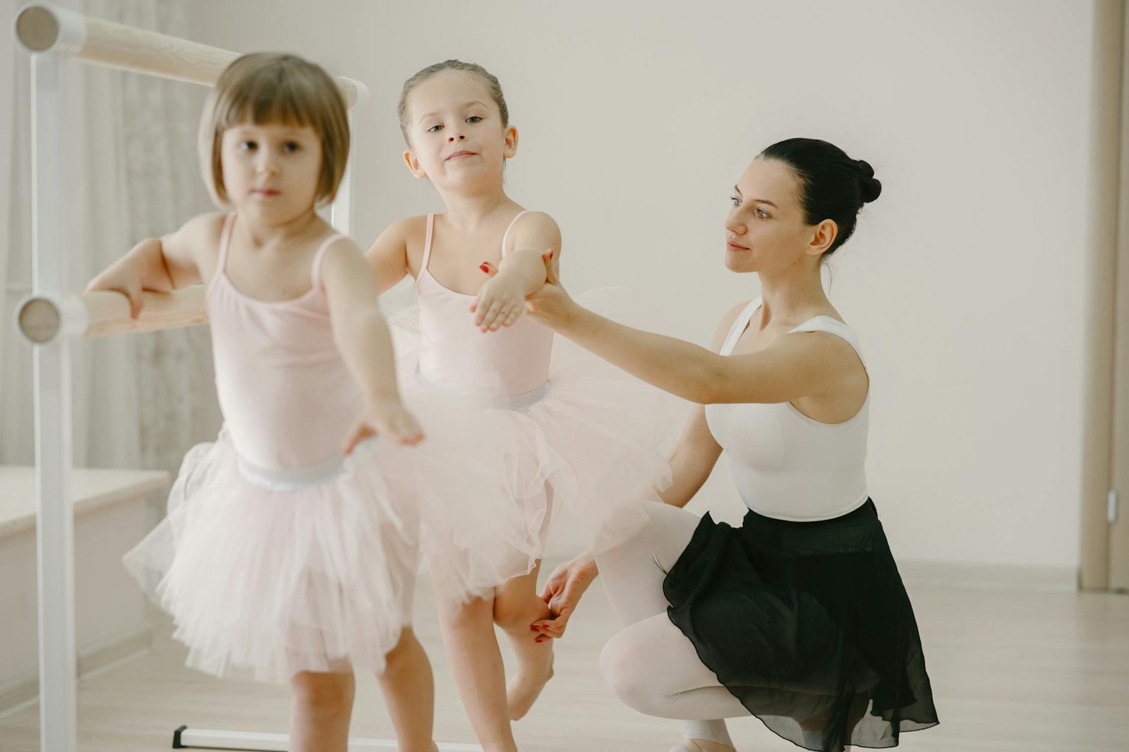 Two young girls in tutus learn ballet with guidance from their instructor in a dance studio.