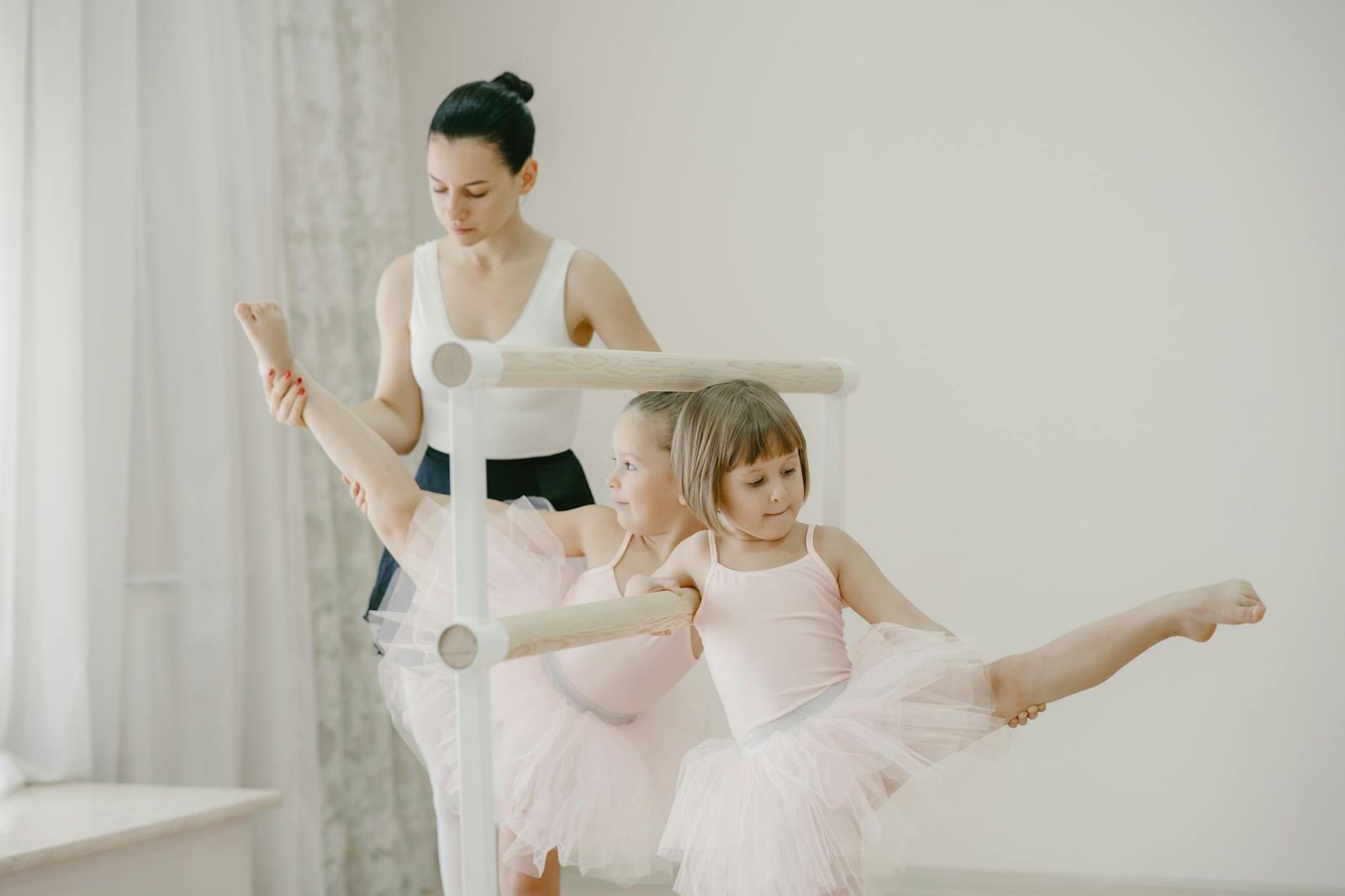 Ballet class with young girls in tutus practicing at the barre, guided by their teacher.