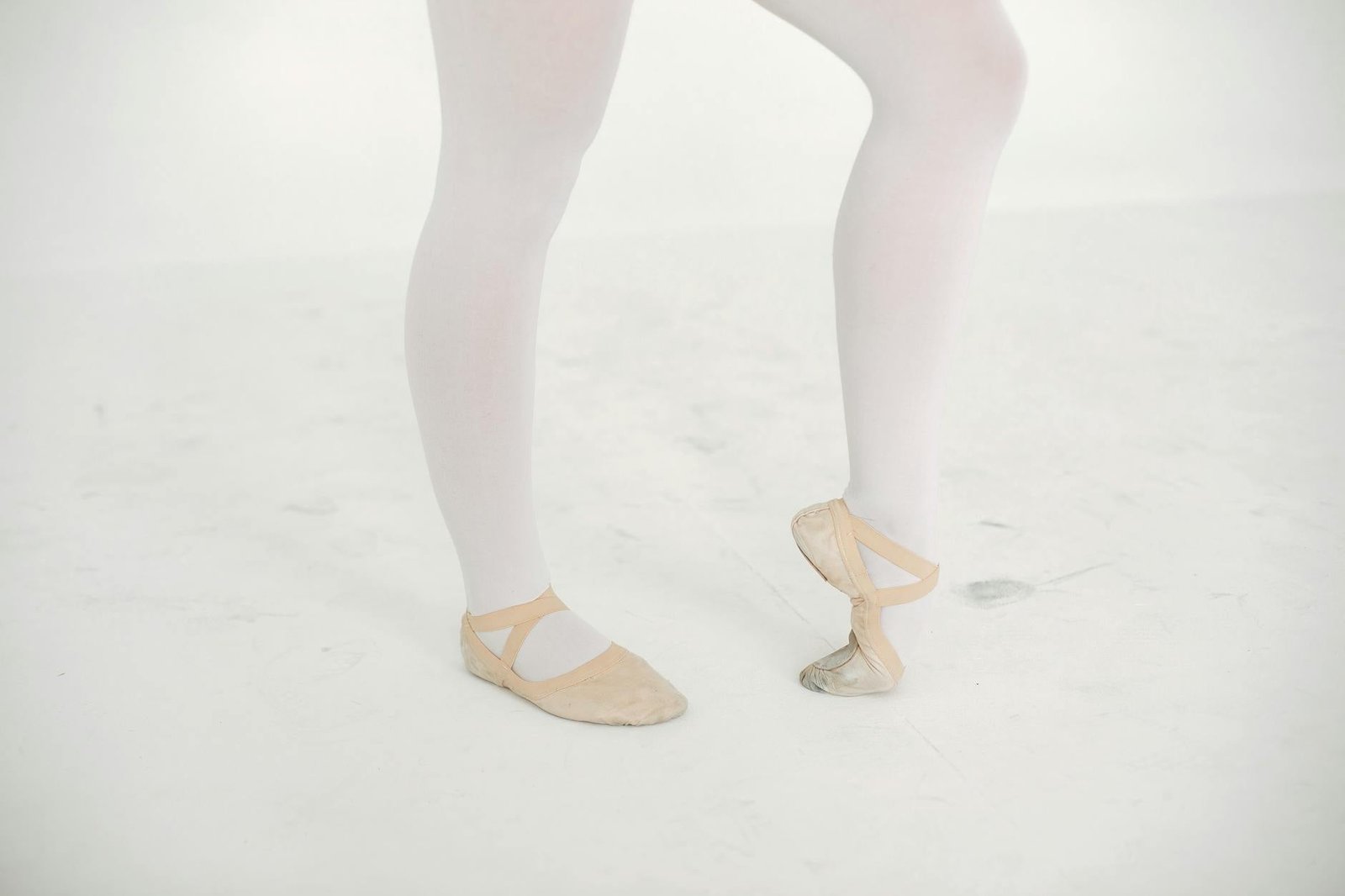 A detailed view of a ballerina's feet in ballet shoes on a pristine white background.