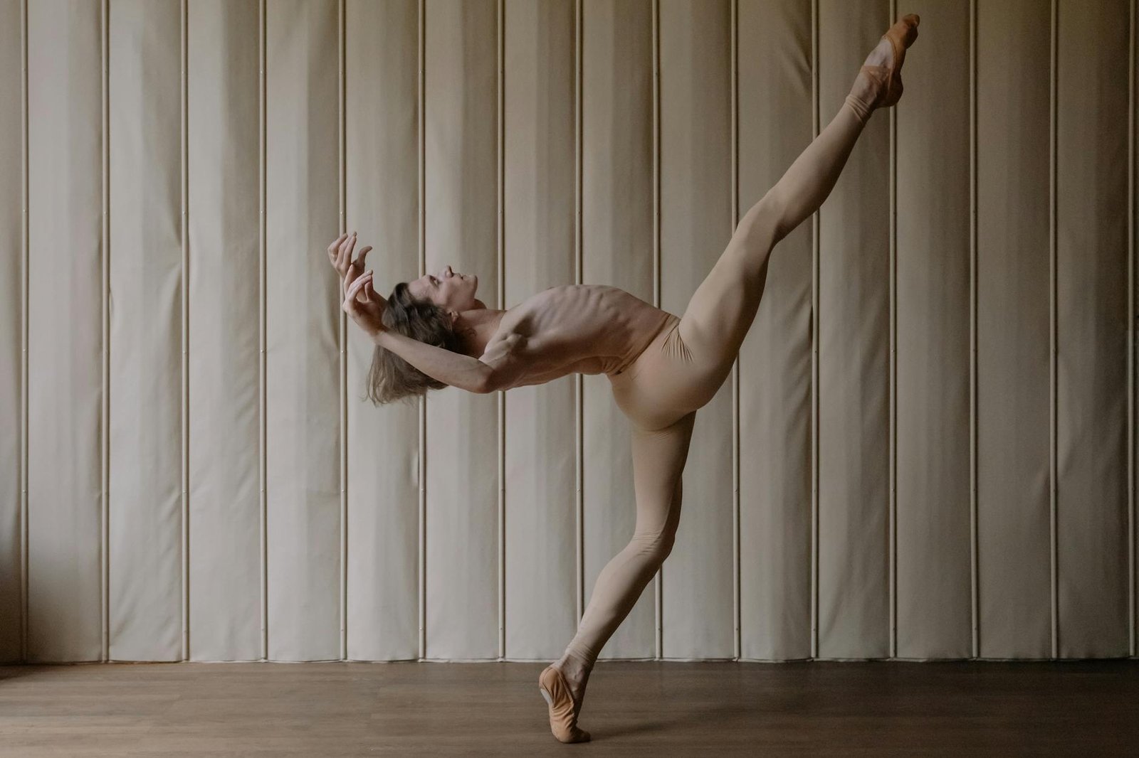 Male ballet dancer in pose indoors, showcasing grace and flexibility in nude tones.