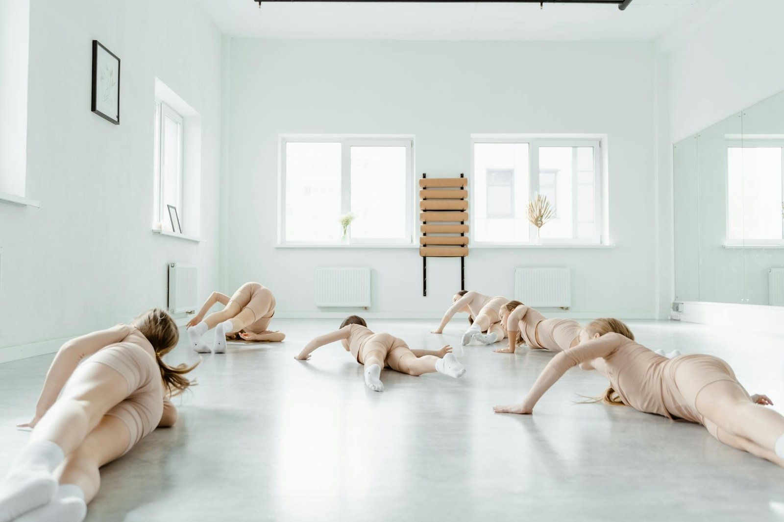 Group of young dancers practicing ballet choreography on the floor in a bright studio.