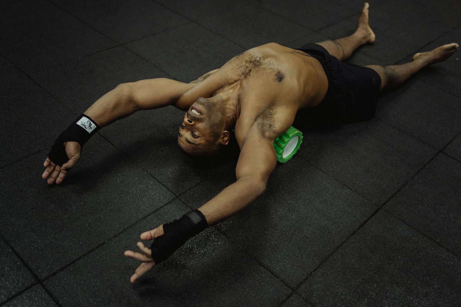 Topless man using foam roller for muscle recovery in gym setting.