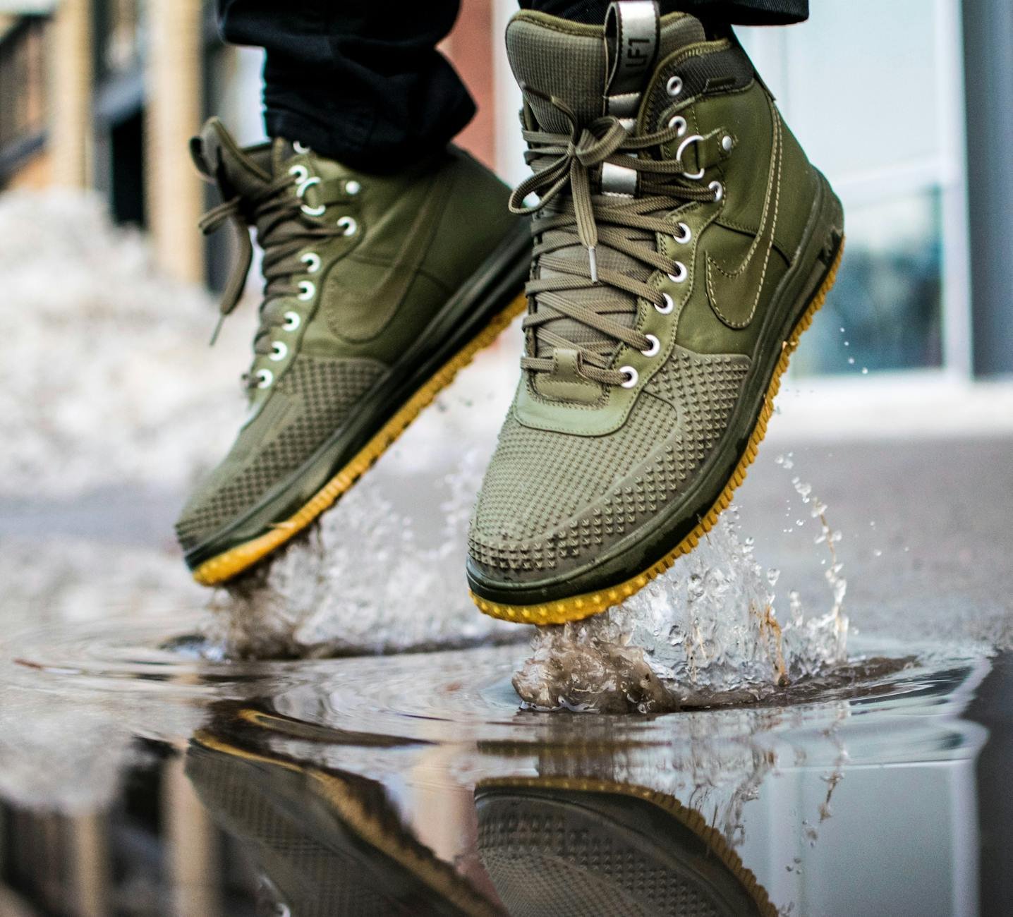 Close-up of green sneakers jumping in a puddle splashing water.