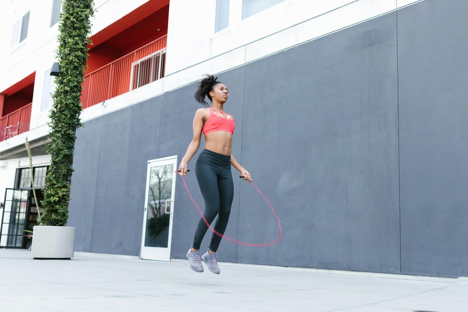 Fit woman with curly hair exercising outdoors by skipping rope. Focus on fitness and motion.