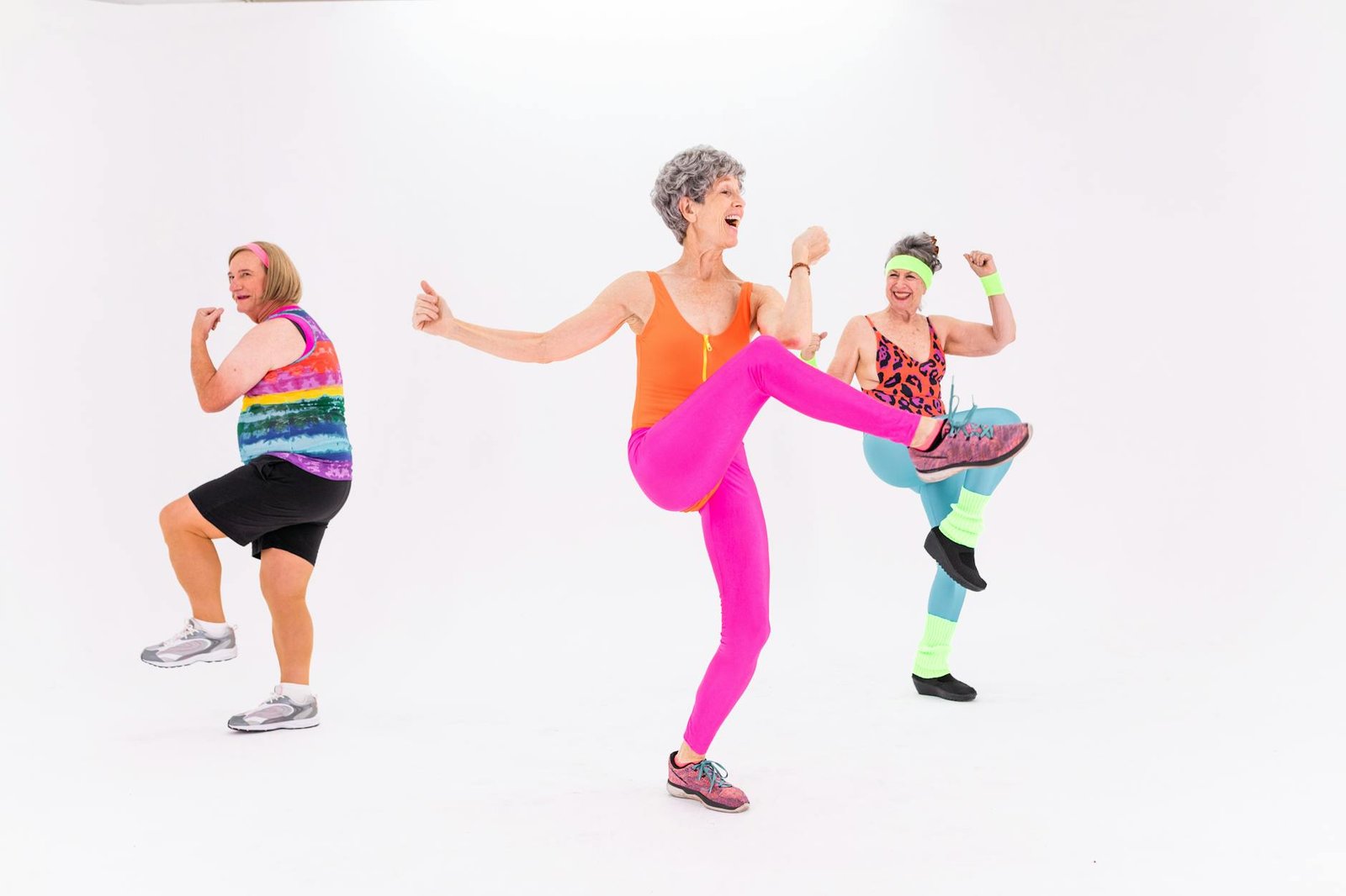 Three senior women having fun and staying fit with energetic aerobics in colorful outfits indoors.