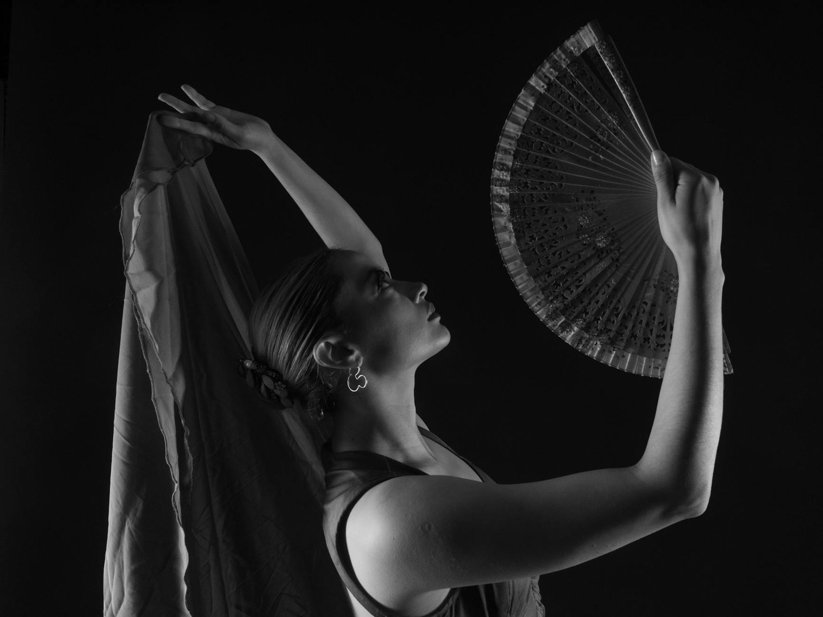 Black and white photo of a flamenco dancer with a fan in a graceful pose, capturing elegance and movement.