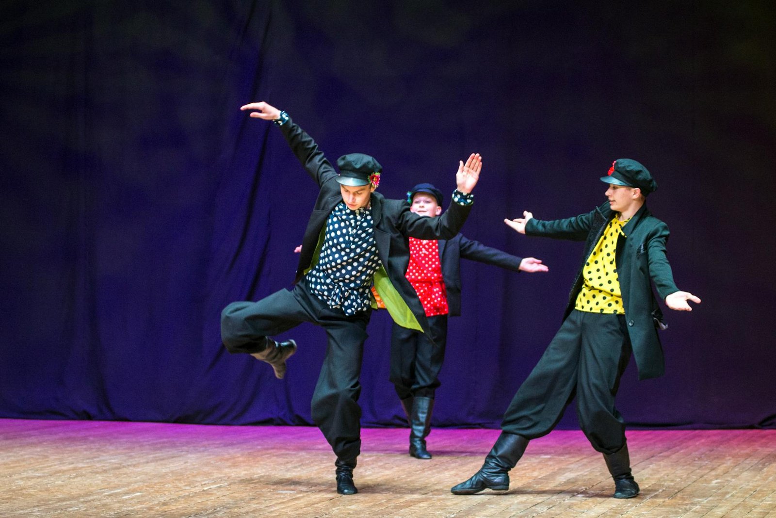 Vibrant folk dance performance by three young male performers on stage.