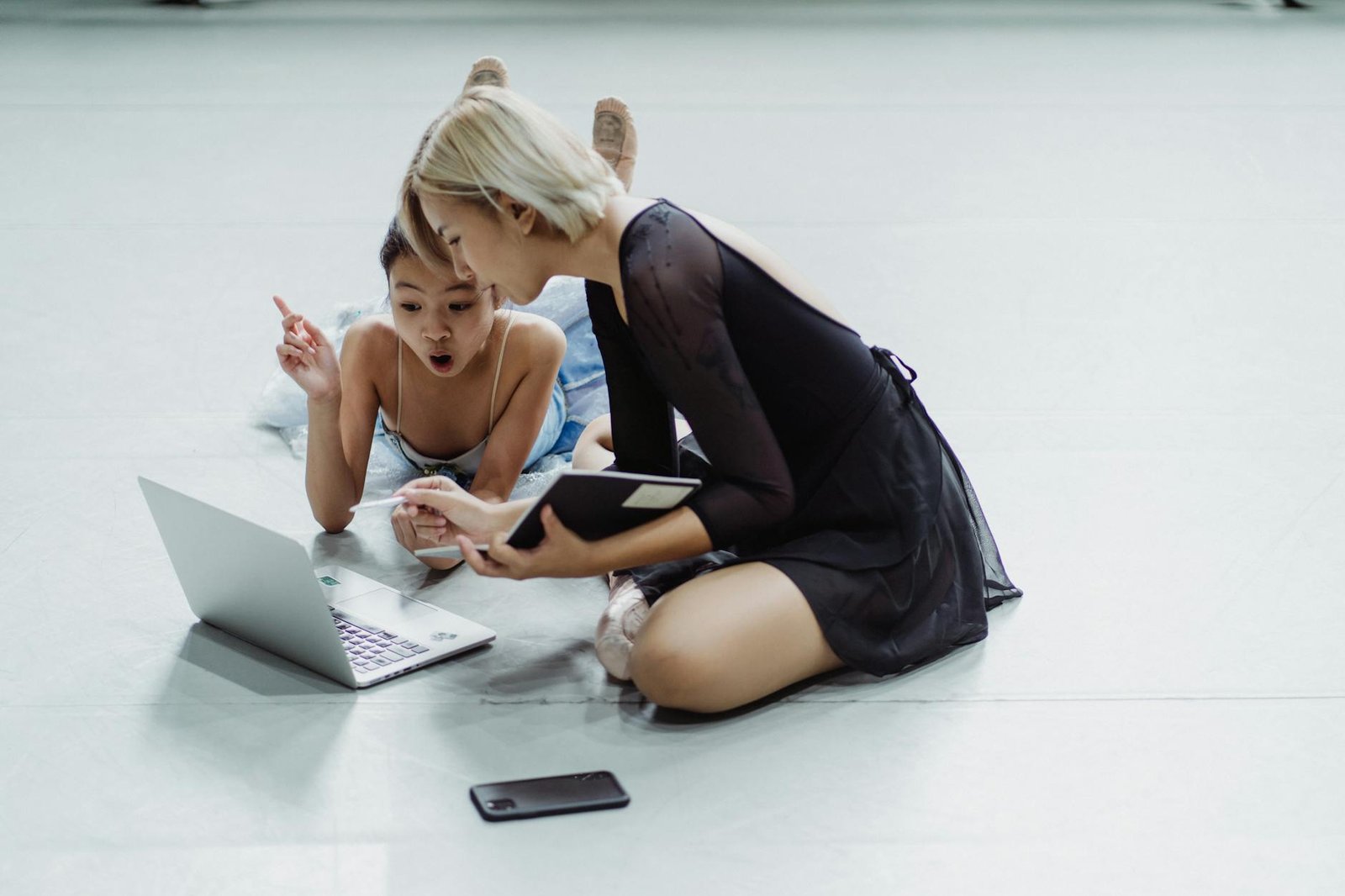 From above full length of ethnic amazed girl browsing netbook with personal coach holding notebook in ballet class