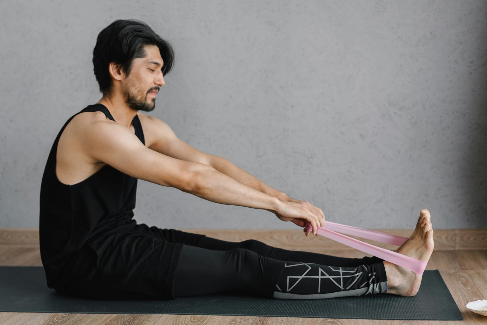 Adult man performing stretching exercises with a resistance band on a yoga mat indoors for fitness and wellness.