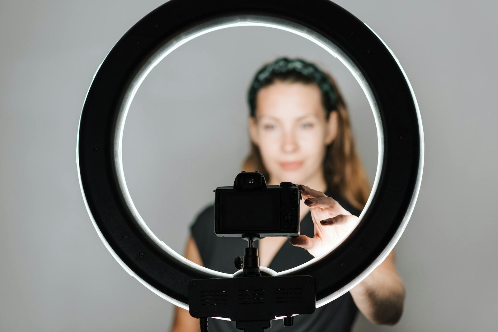 Young female taking self portrait with modern photo camera and studio lamp on white background