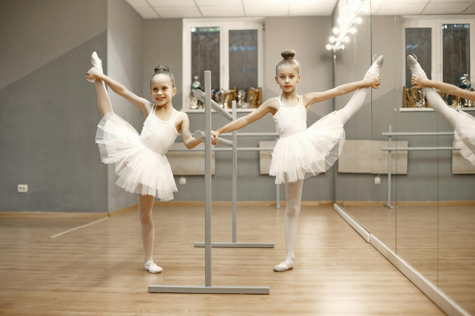Two young ballerinas practicing their moves in a bright ballet studio.