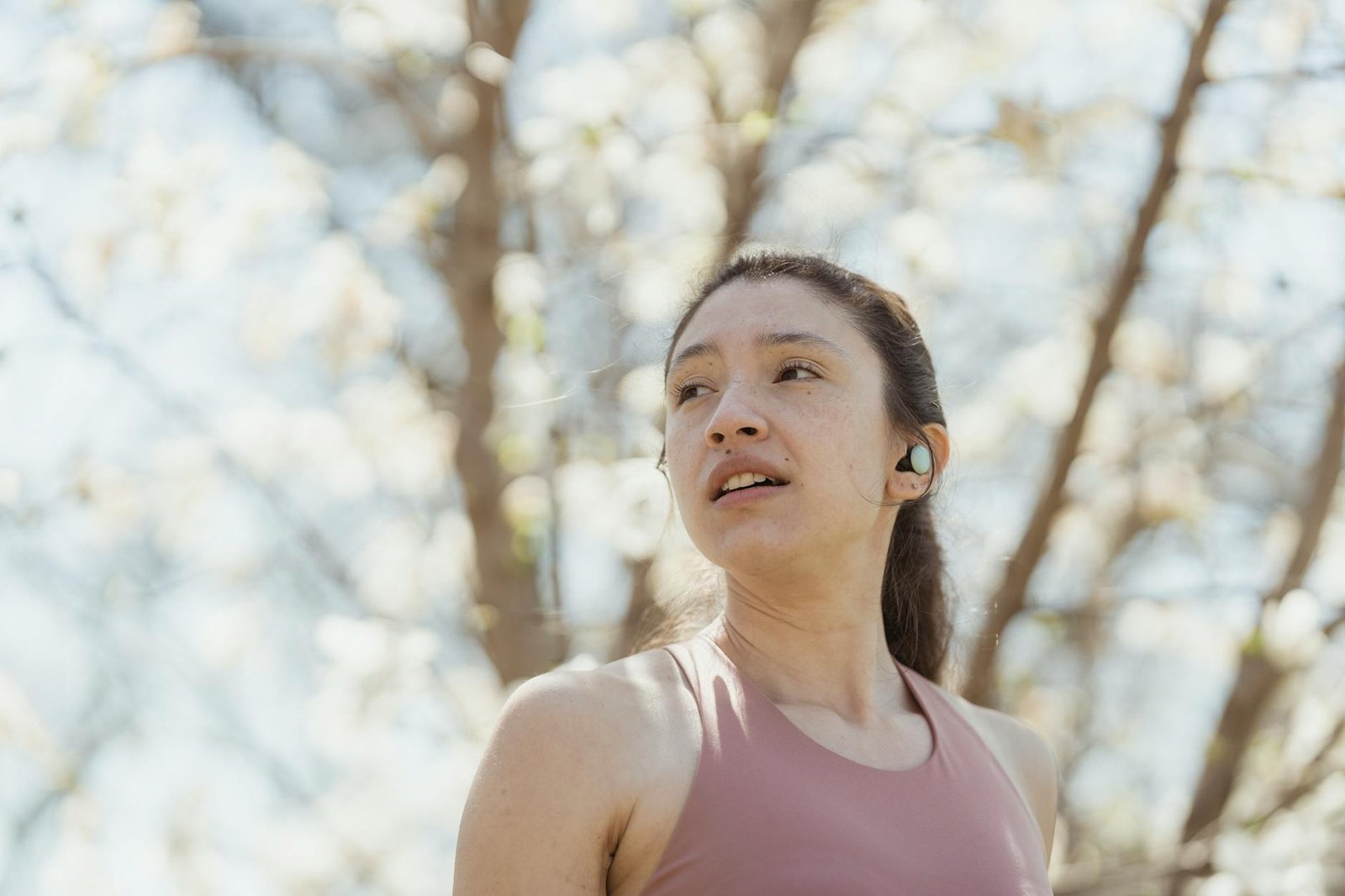 Woman jogging in a park with wireless earbuds during a sunny spring day.