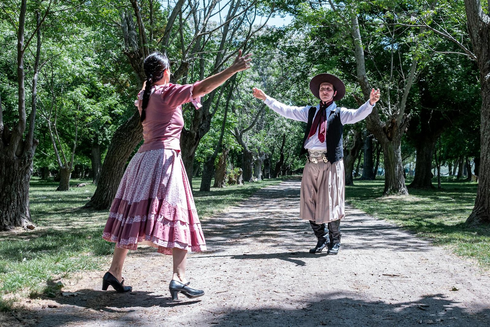Gaucho dancers in traditional attire performing in a lush park setting in Chascomús, Argentina.