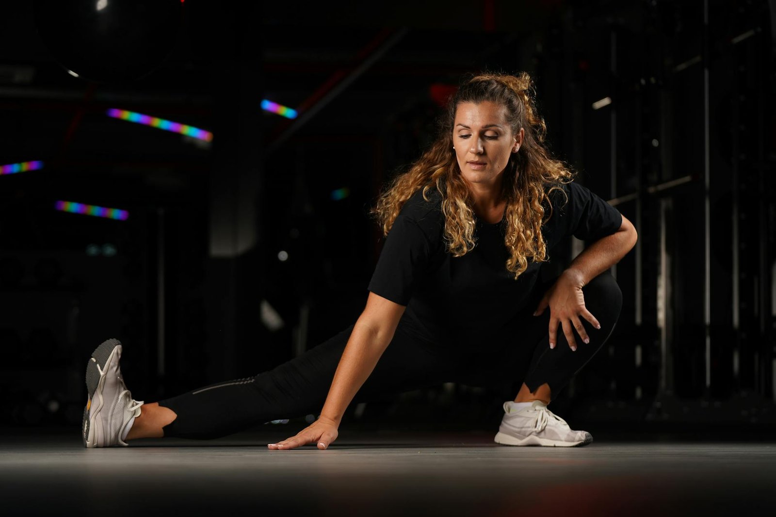 Woman stretching in a dimly lit gym in Riga, Latvia, focused on flexibility.