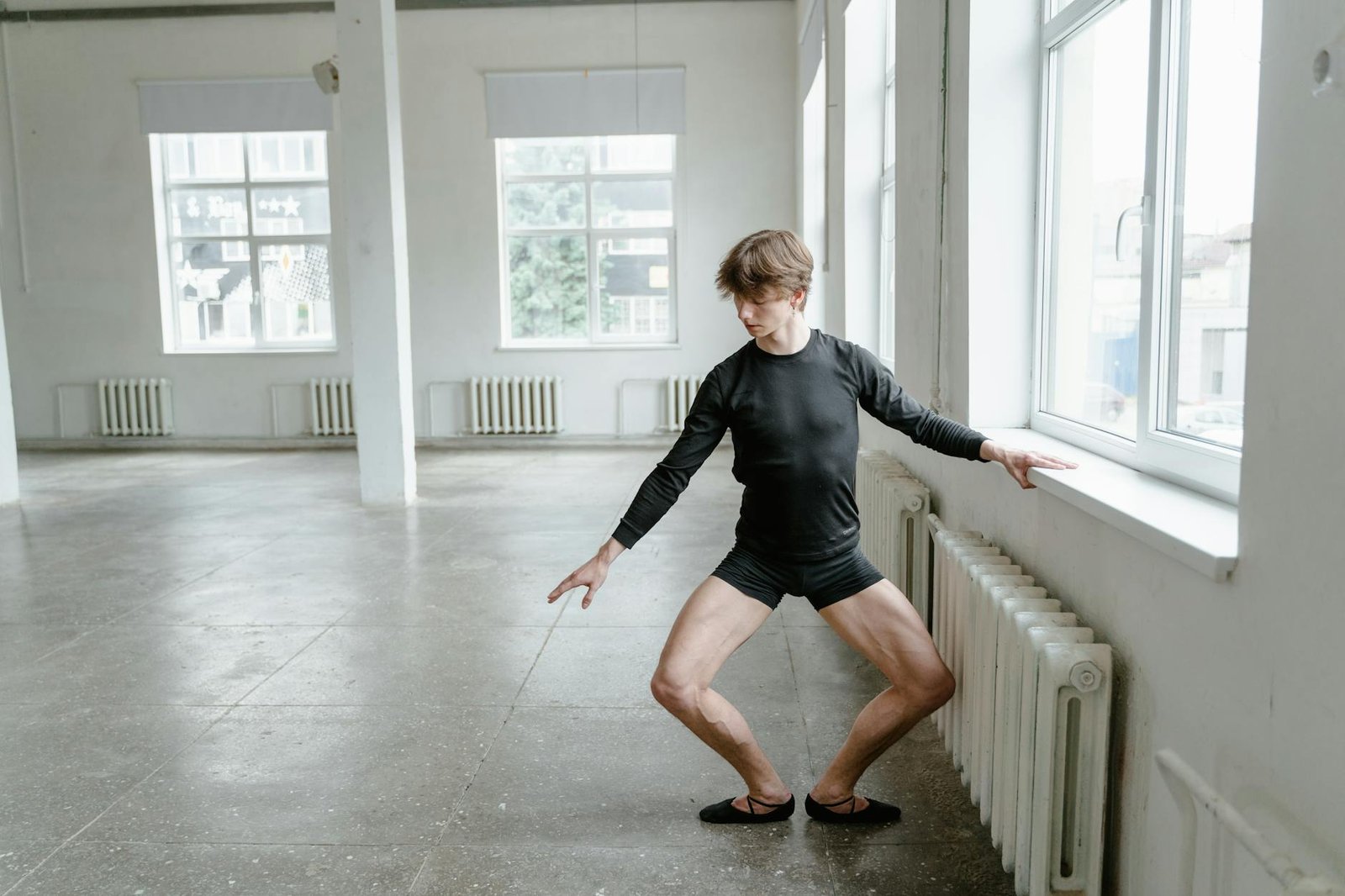 Professional male ballet dancer rehearsing near window in bright studio.