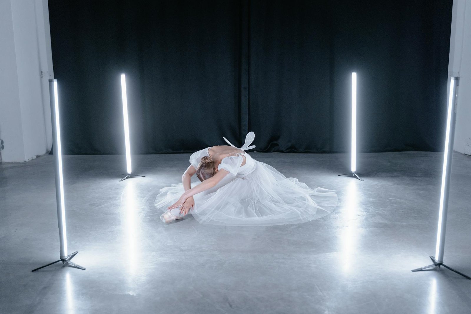 Ballet dancer in a white dress practicing stretching in a professional studio.