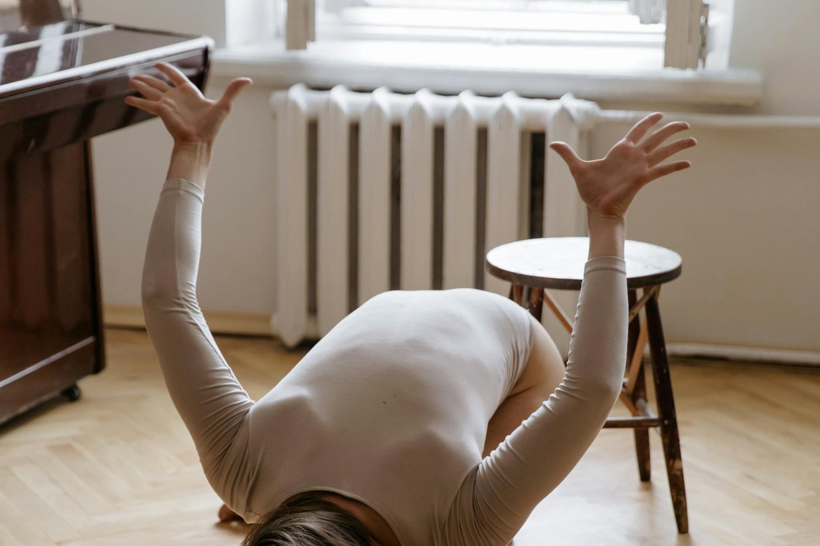 A woman in a bodysuit strikes a contemporary dance pose indoors, showcasing flexibility.