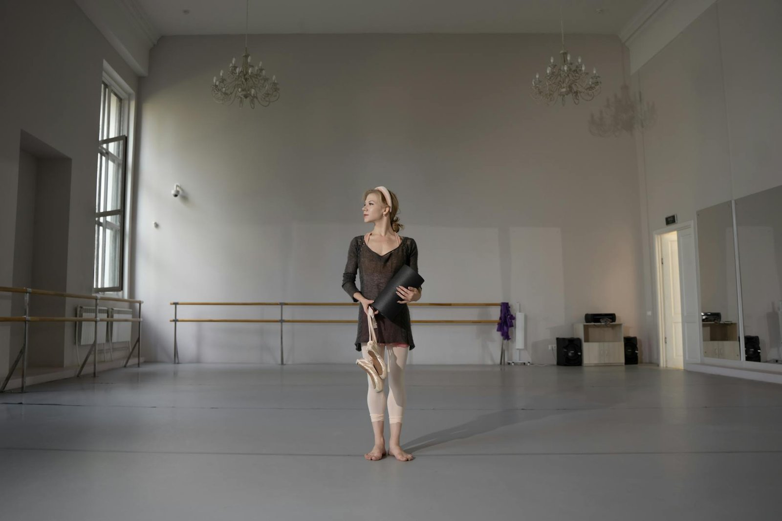 Ballet dancer holding pointe shoes and mat in elegant studio.