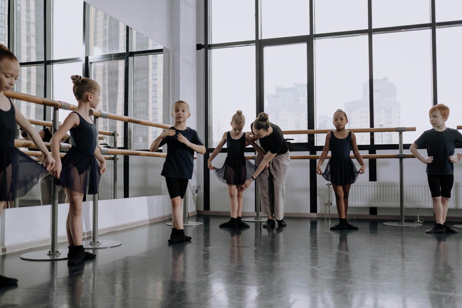 Ballet instructor teaching children in an indoor dance studio setting.