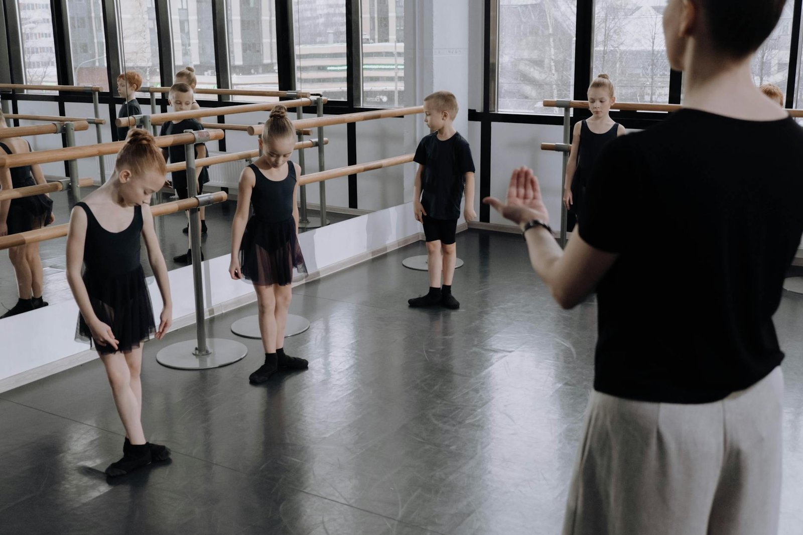 Young ballet students practicing in a bright studio with an instructor guiding them.