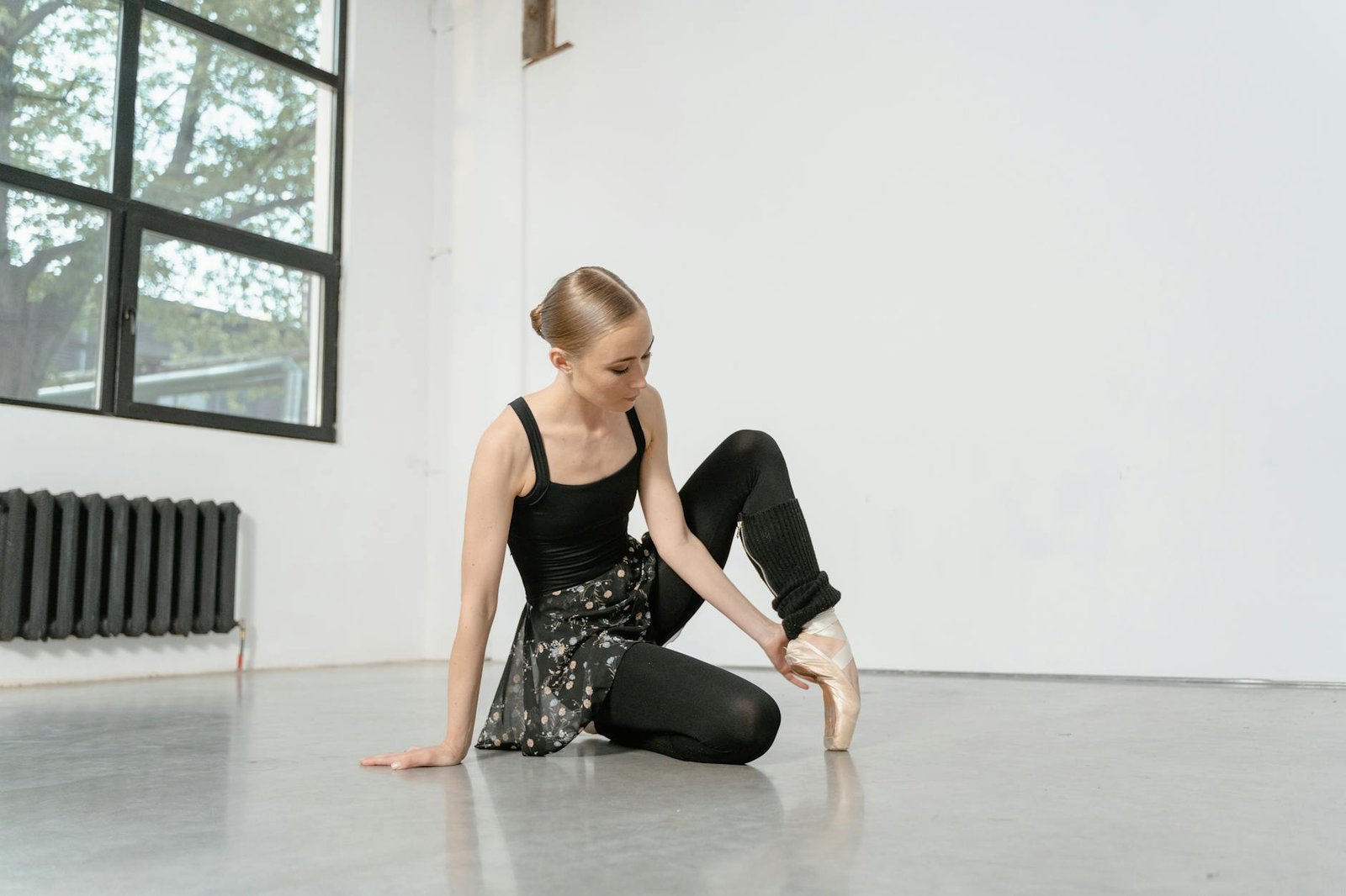 Young ballerina in black attire practicing on pointe shoes in a bright dance studio.