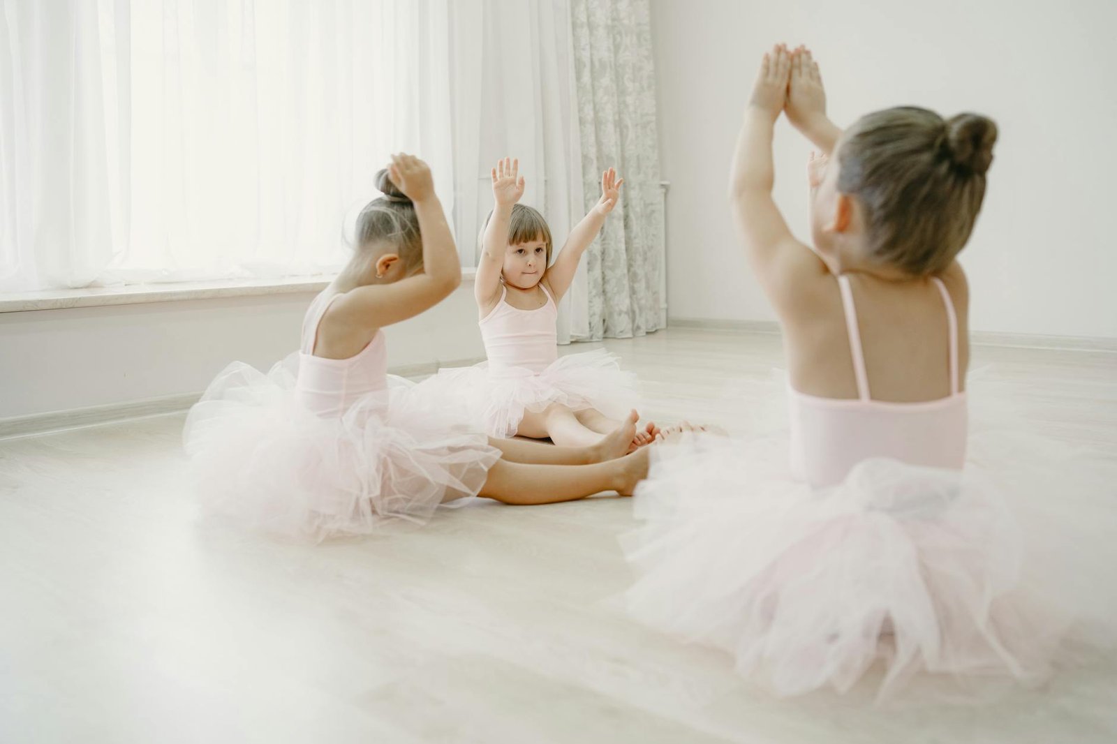 Three young ballet dancers in a dance class practicing poses, wearing tutus.