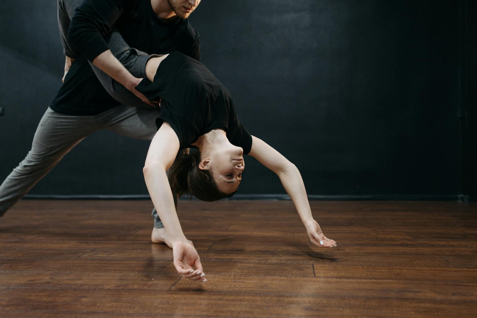 A man and woman performing dynamic dance moves on a wooden floor indoors.