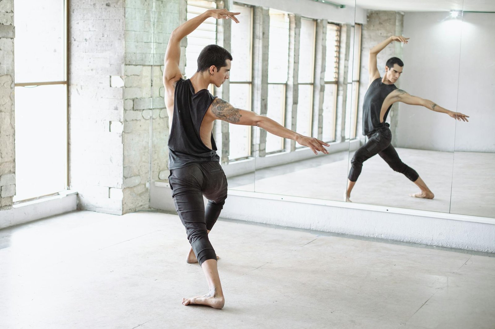 A male ballet dancer rehearses in a bright dance studio, focusing on his reflection.