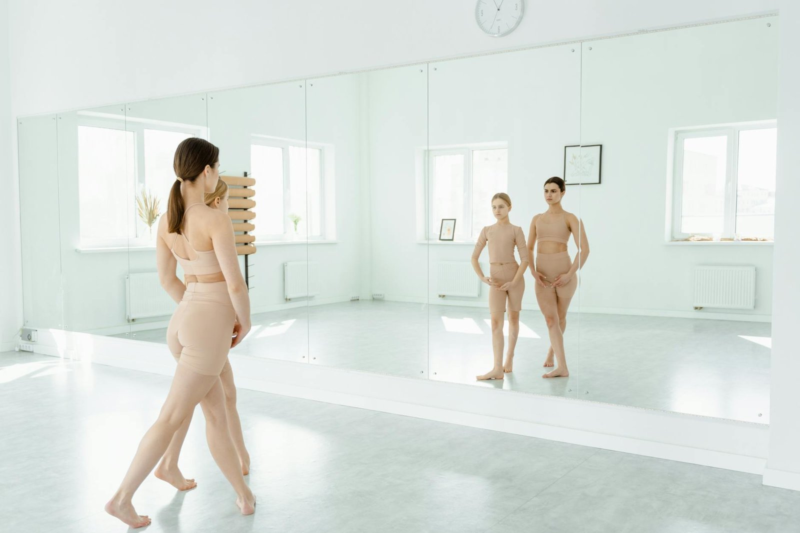 Two female dancers in a bright ballet studio practicing in front of a mirror.