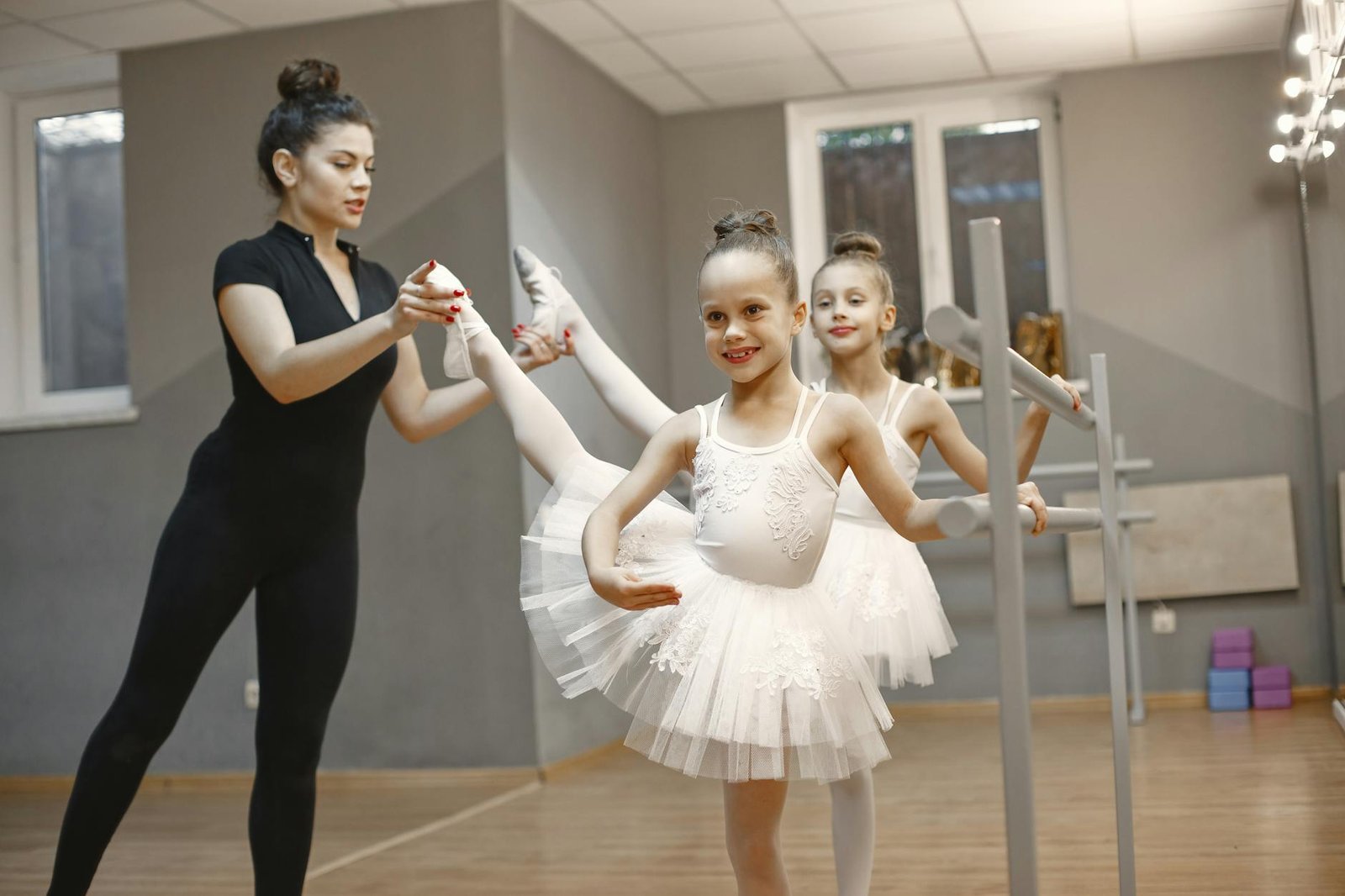 Children learning ballet with a teacher, wearing tutus, in a studio setting.