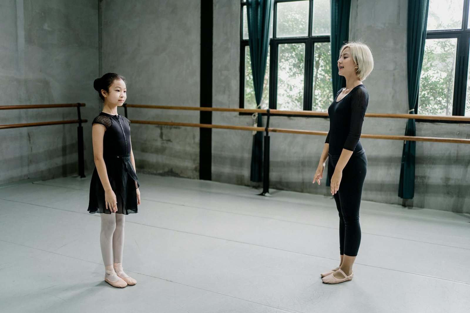 Side view full length Asian female ballerina trainer and girl ballerina standing straight in spacious light ballet studio