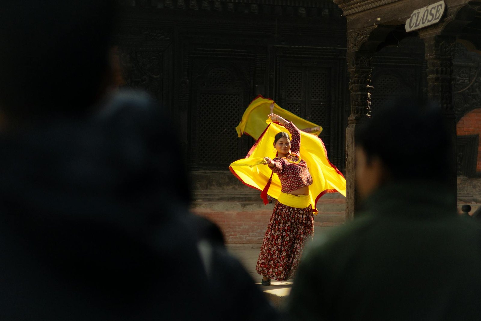 A female dancer performs in traditional attire with vibrant yellow cloth in an outdoor setting.