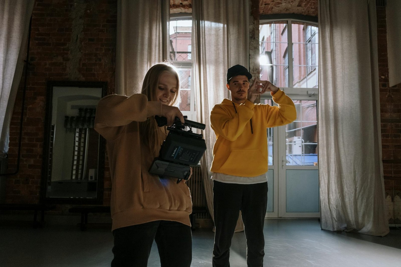Two adults filming creatively indoors with video cameras and warm lighting.