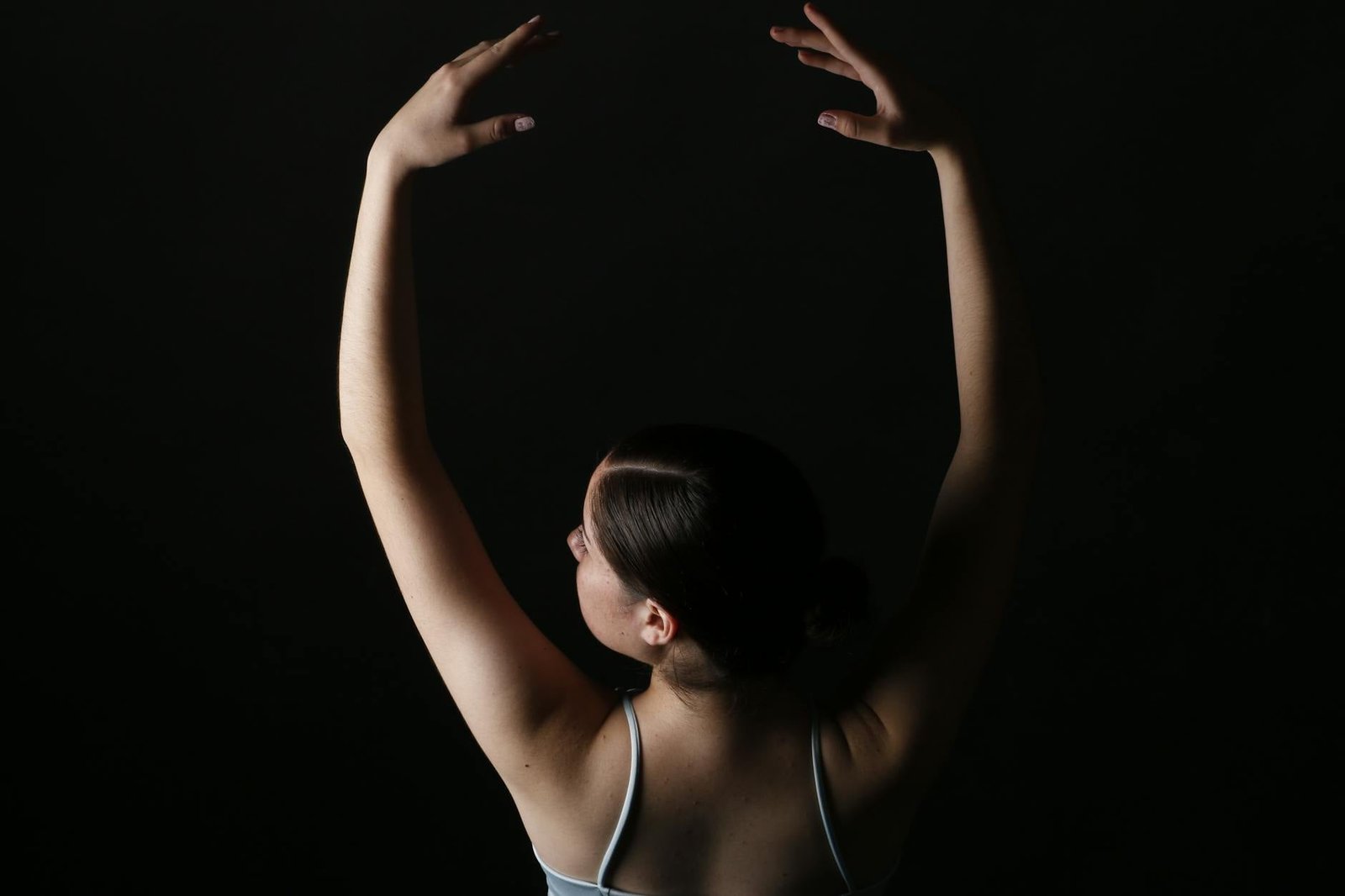 A female ballerina poses gracefully against a dark background in a dance studio, capturing movement and form.